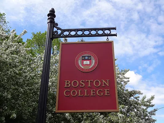 A red Boston College sign against a blue sky.