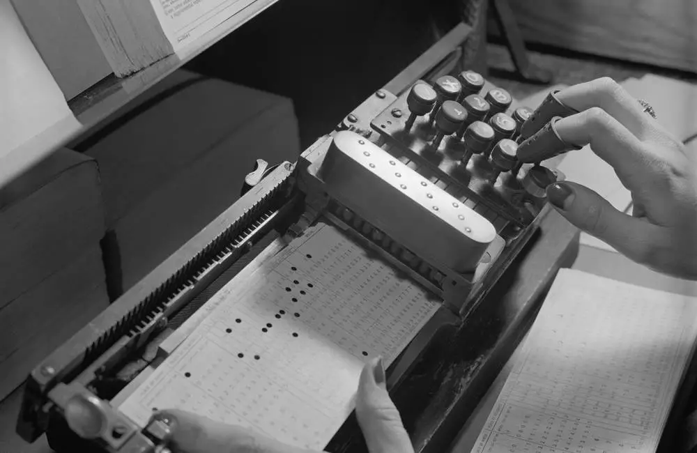 A black and white photo of a hand typing out numbers on an old machine.